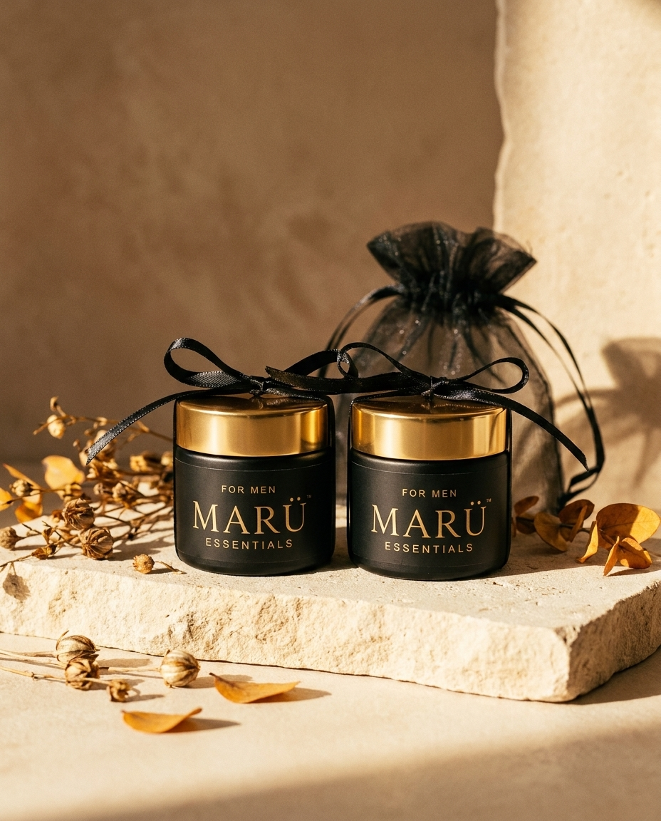Two travel size MARÜ ESSENTIALS jars tied with black ribbon beside an organza pouch on pale stone